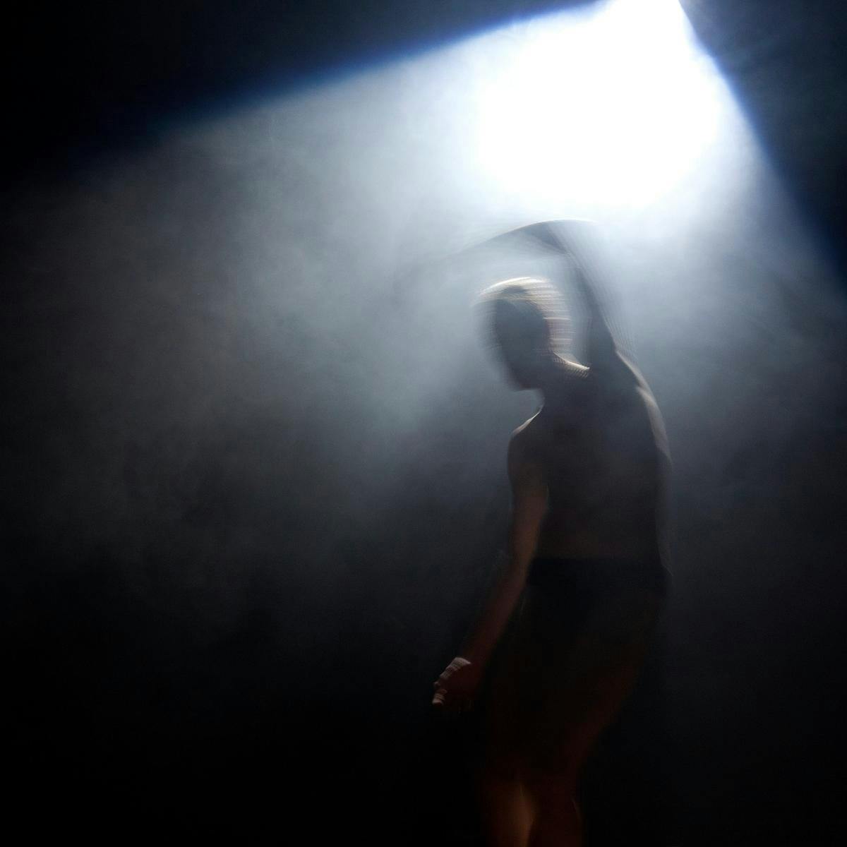 A silhouetted person dancing in a bright white light, fog surrounds the scene.