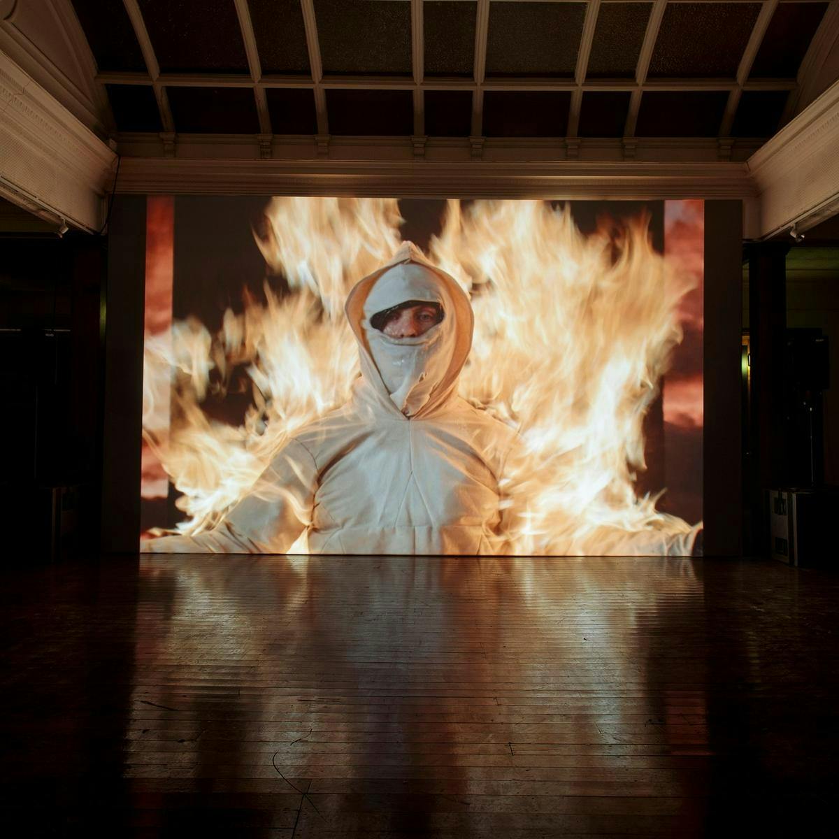 A large screen shows footage of a person wearing a fire-proof suit, they are engulfed in bright orange flames.