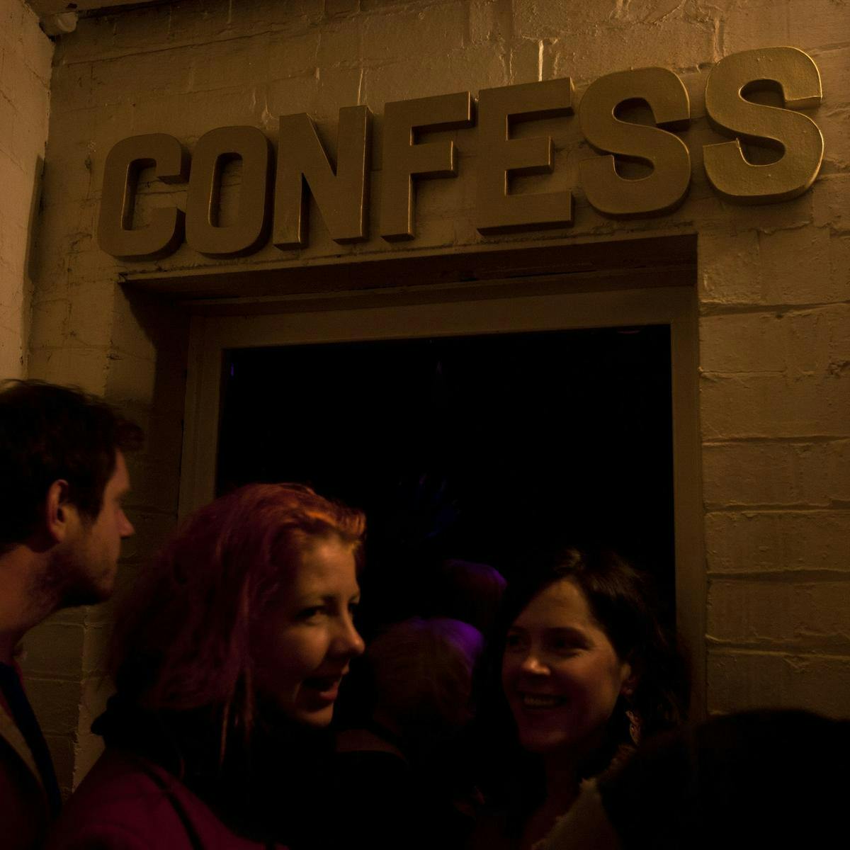 People standing in front of a door with the word 'Confess' written above the doorway.