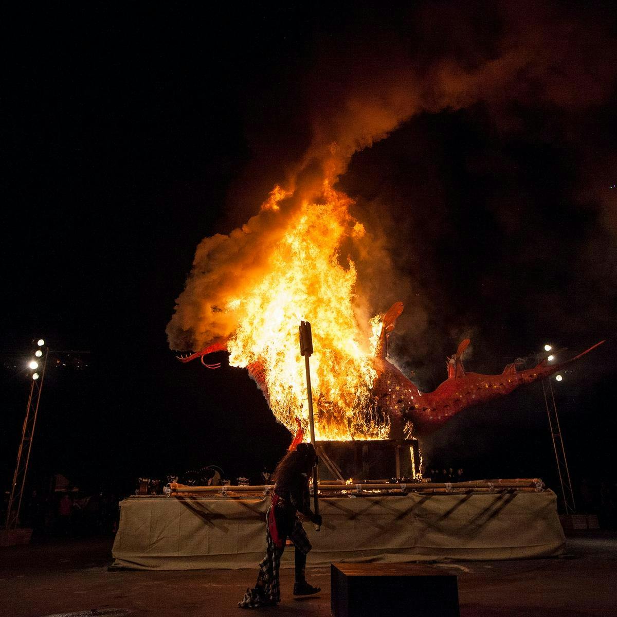 A large seahorse Ogoh-Ogoh is engulfed by bright orange flames as it burns.