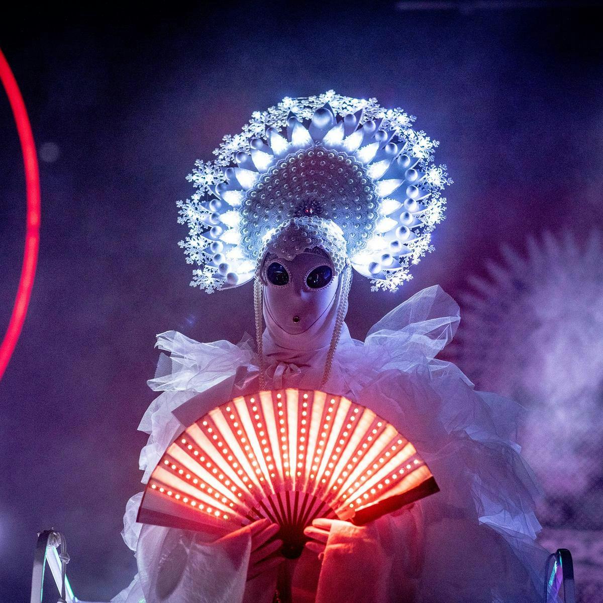 Pope Alice wearing an extravagant white frilly outfit. They hold an ogi style fan in front of them that is lit up orange.