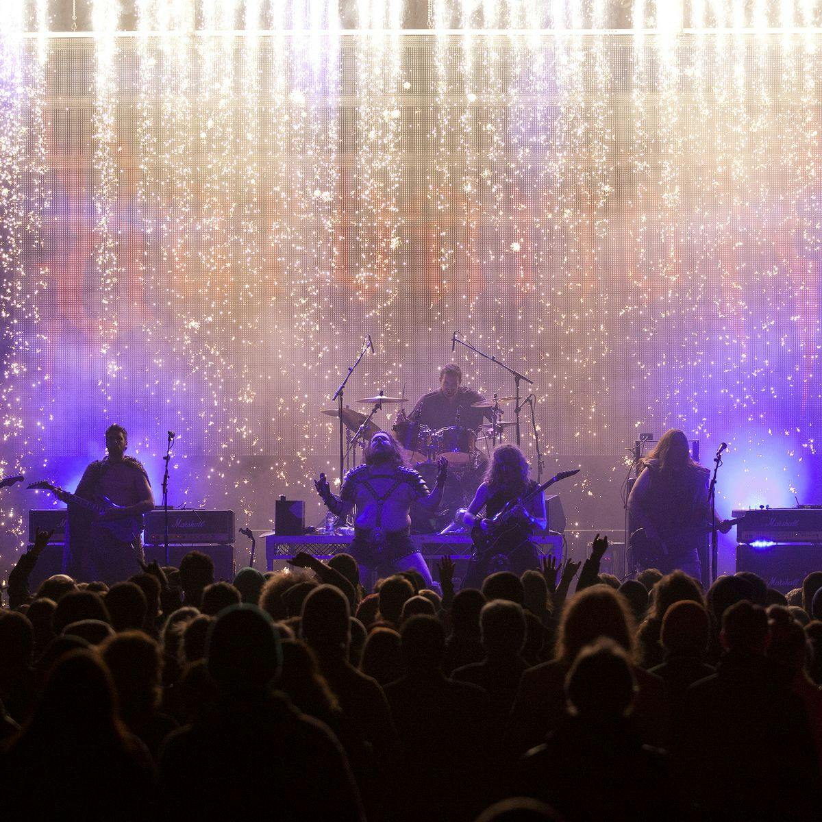 A band performs on stage, whilst a cascade of sparklers descends upon them.