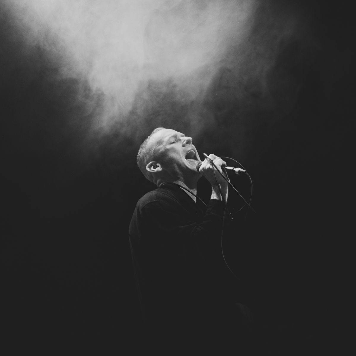 A black and white image of person passionately singing into a microphone.