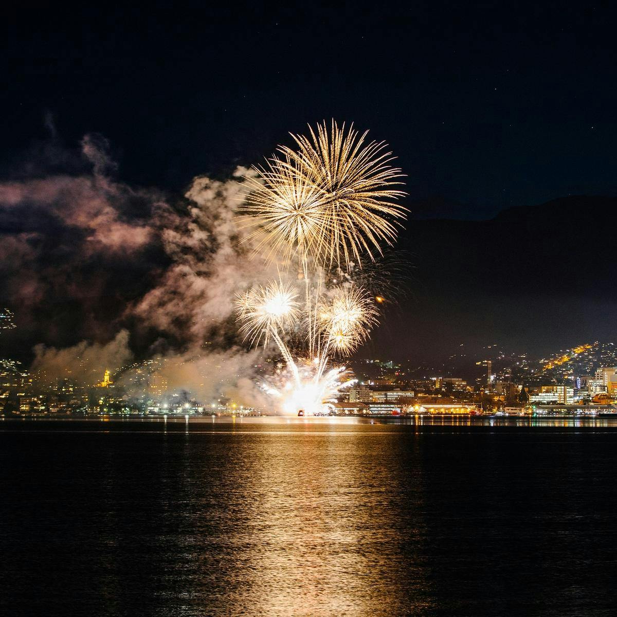 Hobart pictured at night from across River Derwent. Several bright fireworks explode high above the city.