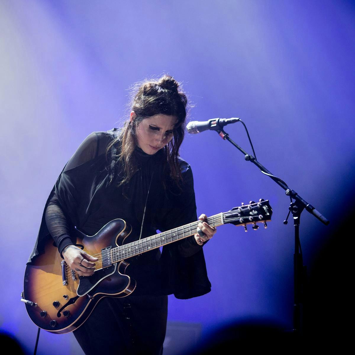 Chelsea Wolfe performs guitar on stage, blue lighting up the background.