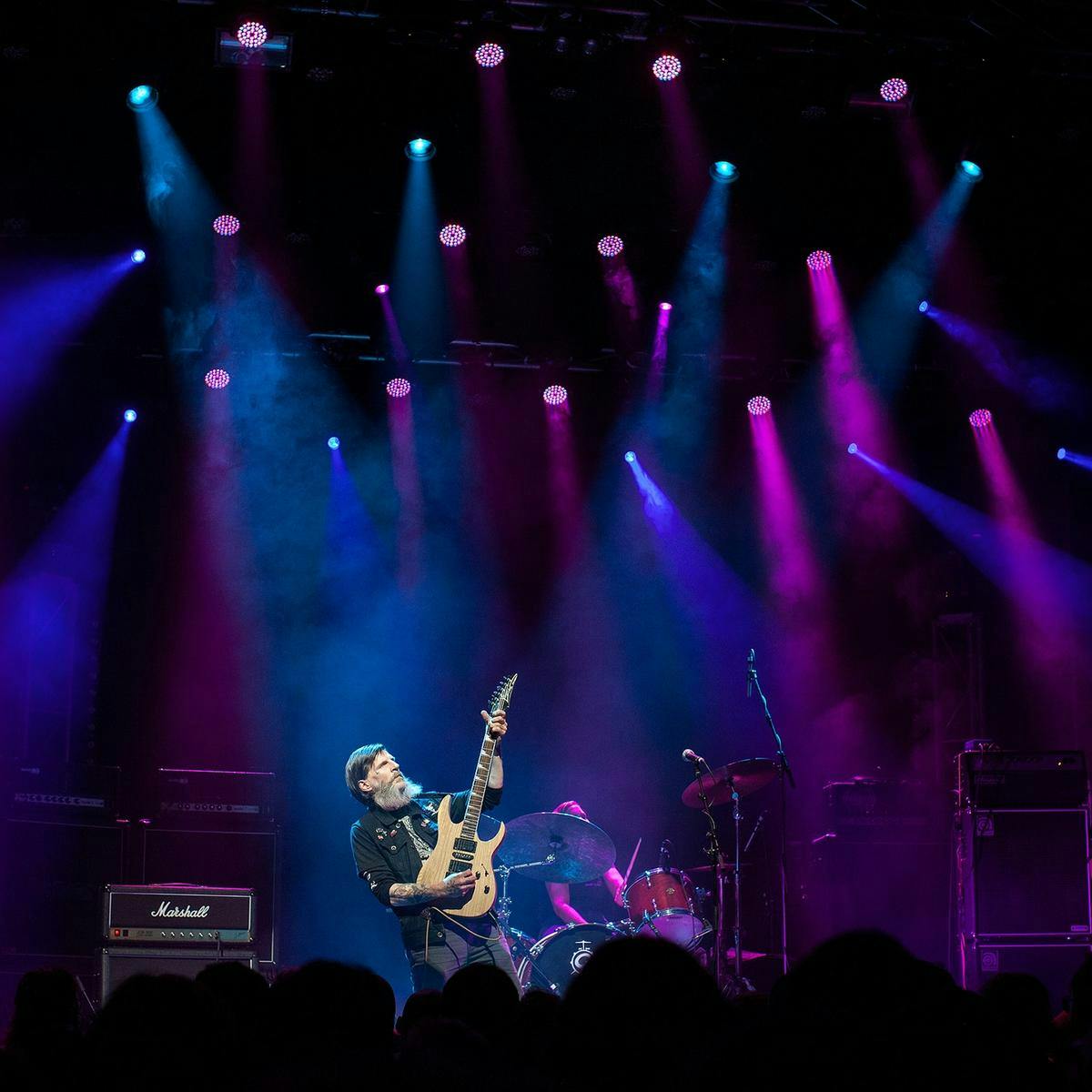 The band Earth performing on-stage, several purple and blue spotlights scour the area.