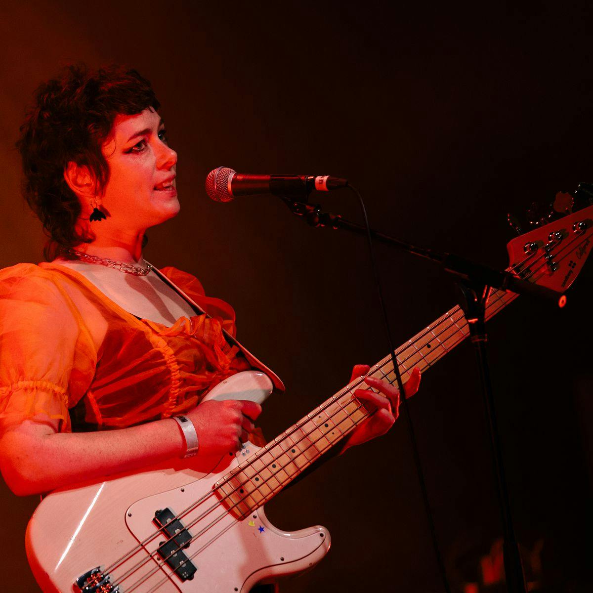 A member of 'Slag Queens' performs on stage with a guitar and microphone.