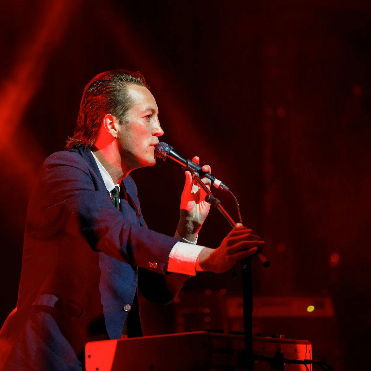 Marlon Williams sings into a microphone, wearing a full suit and tie.