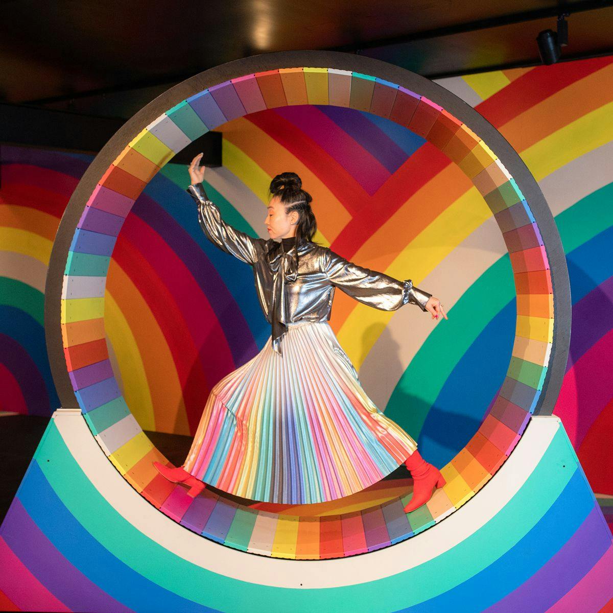 Hiromi Tango poses inside a rainbow hamster wheel at her artwork 'Rainbow Room'. The wheel, and all the walls of the room are painted like rainbows.