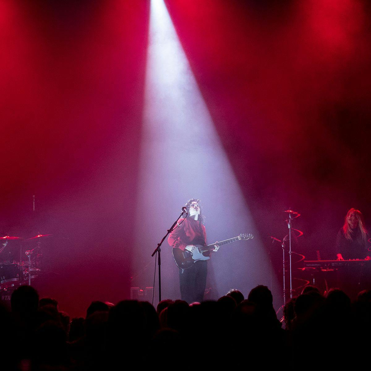 Several musicians perform for a crowd, red and white lights up the stage.