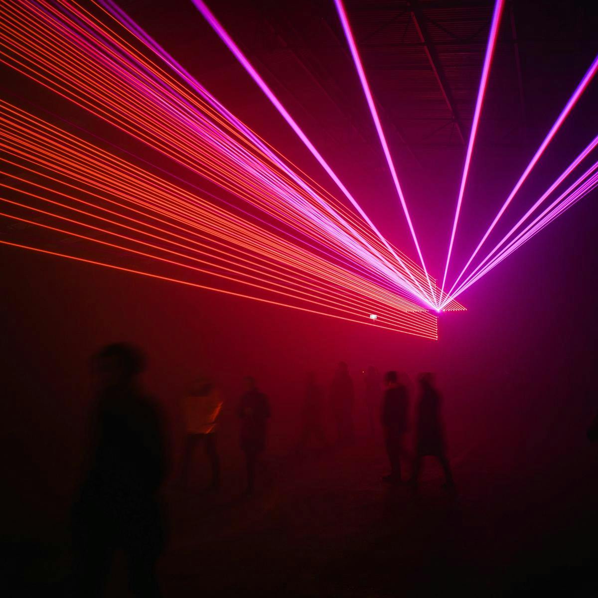 Several people stand in a hazy room, red and purple lasers pierce through the darkness.