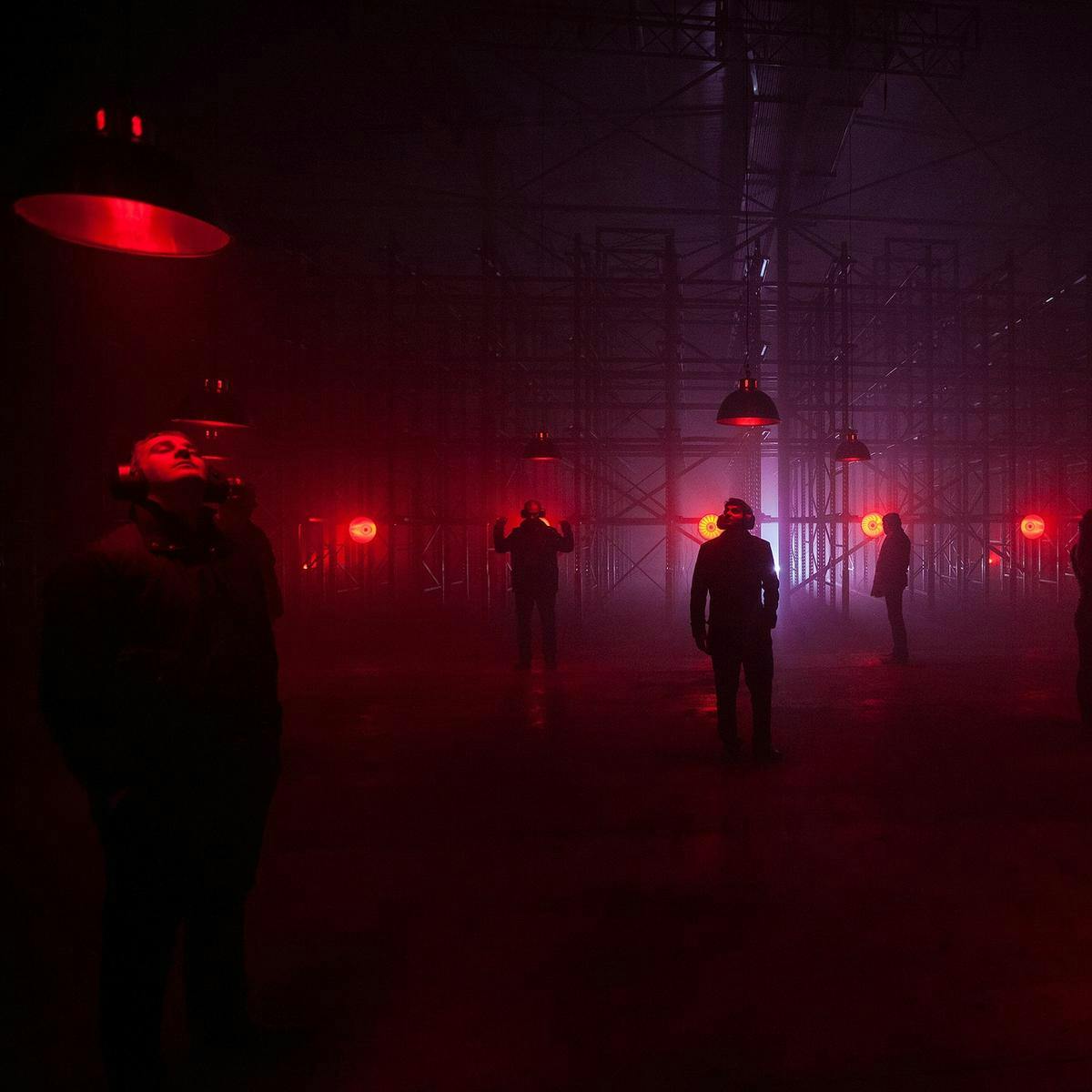 Several people wearing headphones stand below red lights at the 'Bass Bath' artwork. In the background there is a large scaffold structure.