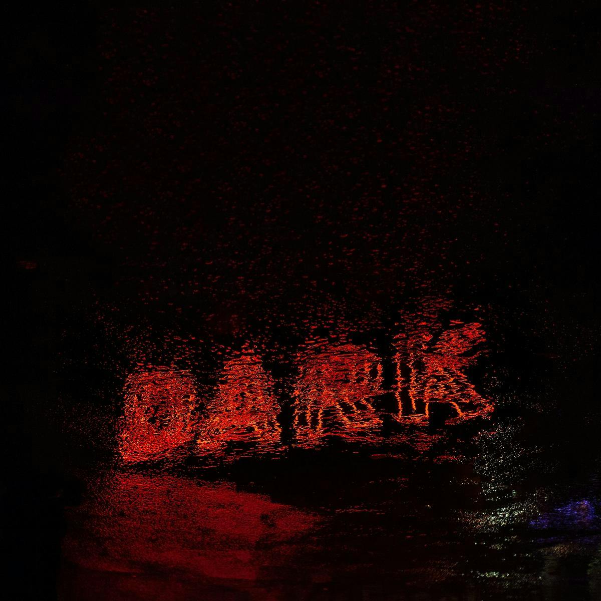 A fuzzy reflection in a puddle of water, of a red neon sign that reads 'Dark'.