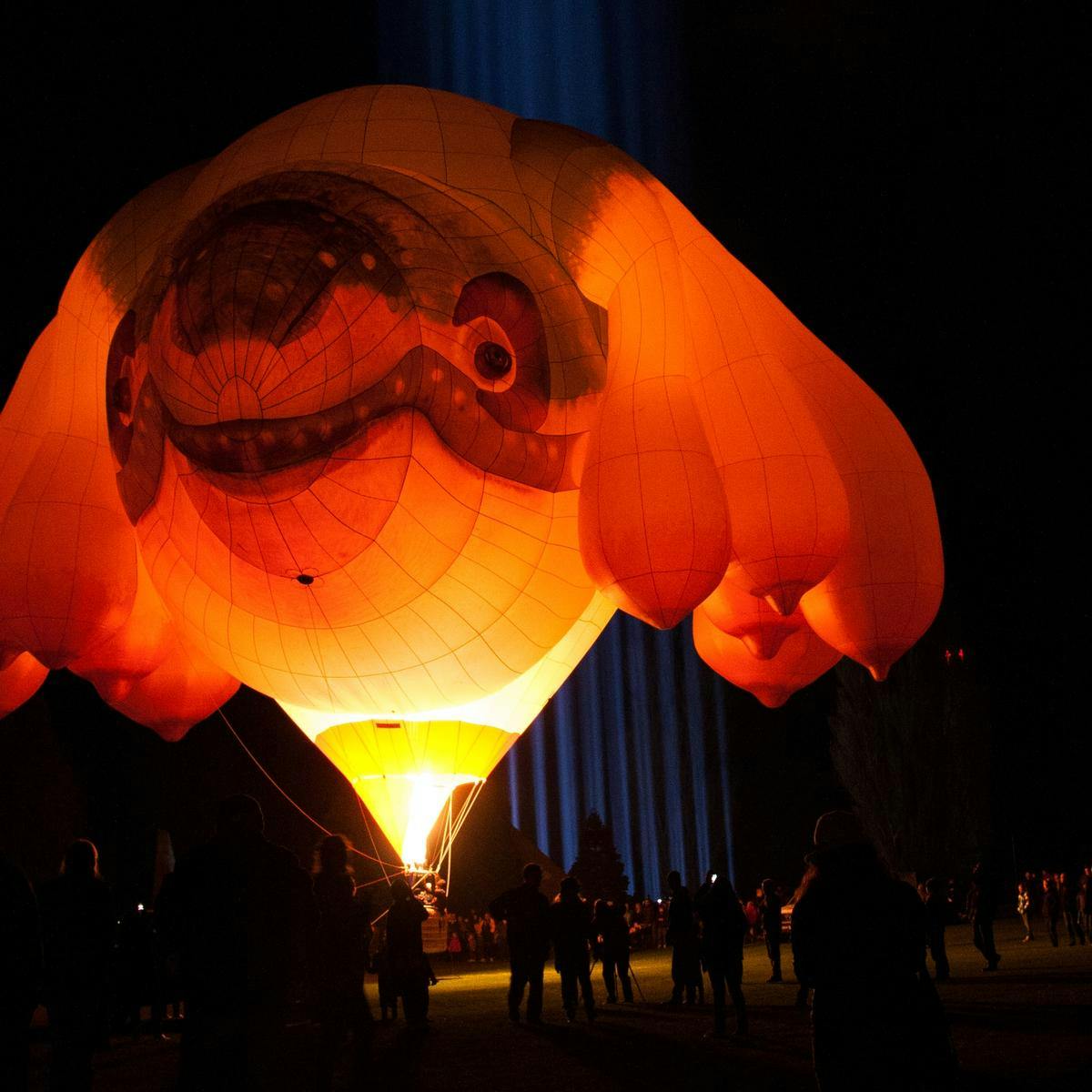 A huge inflatable, hot air balloon-like whale, behind it 'spectra' beams into the night's sky.