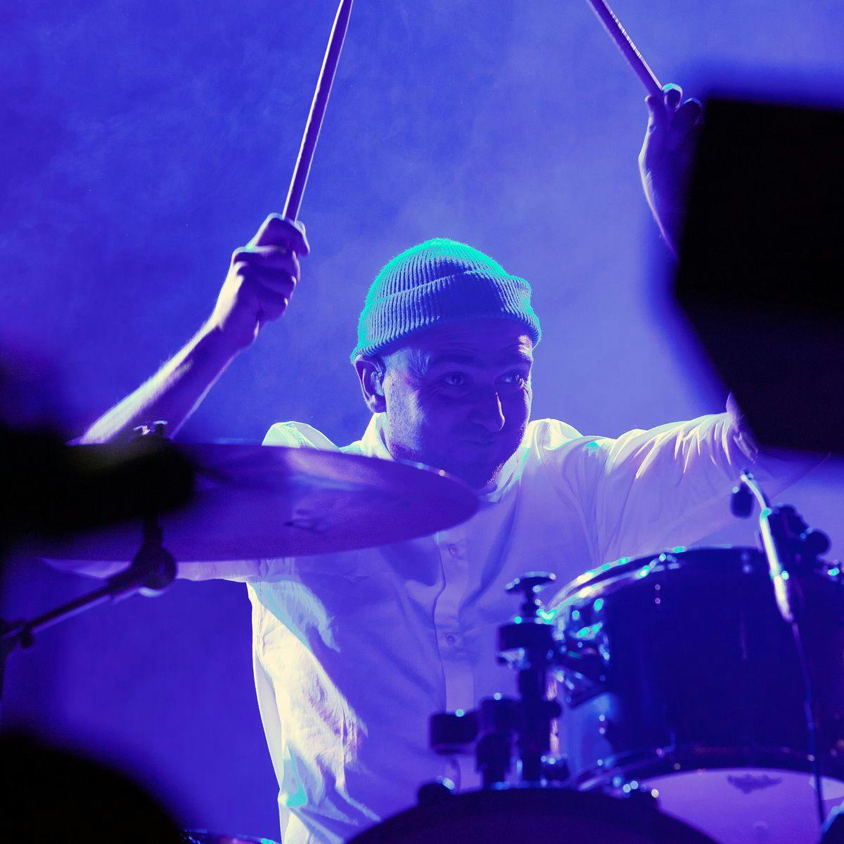 A drummer mid-performance with his sticks held in the air.