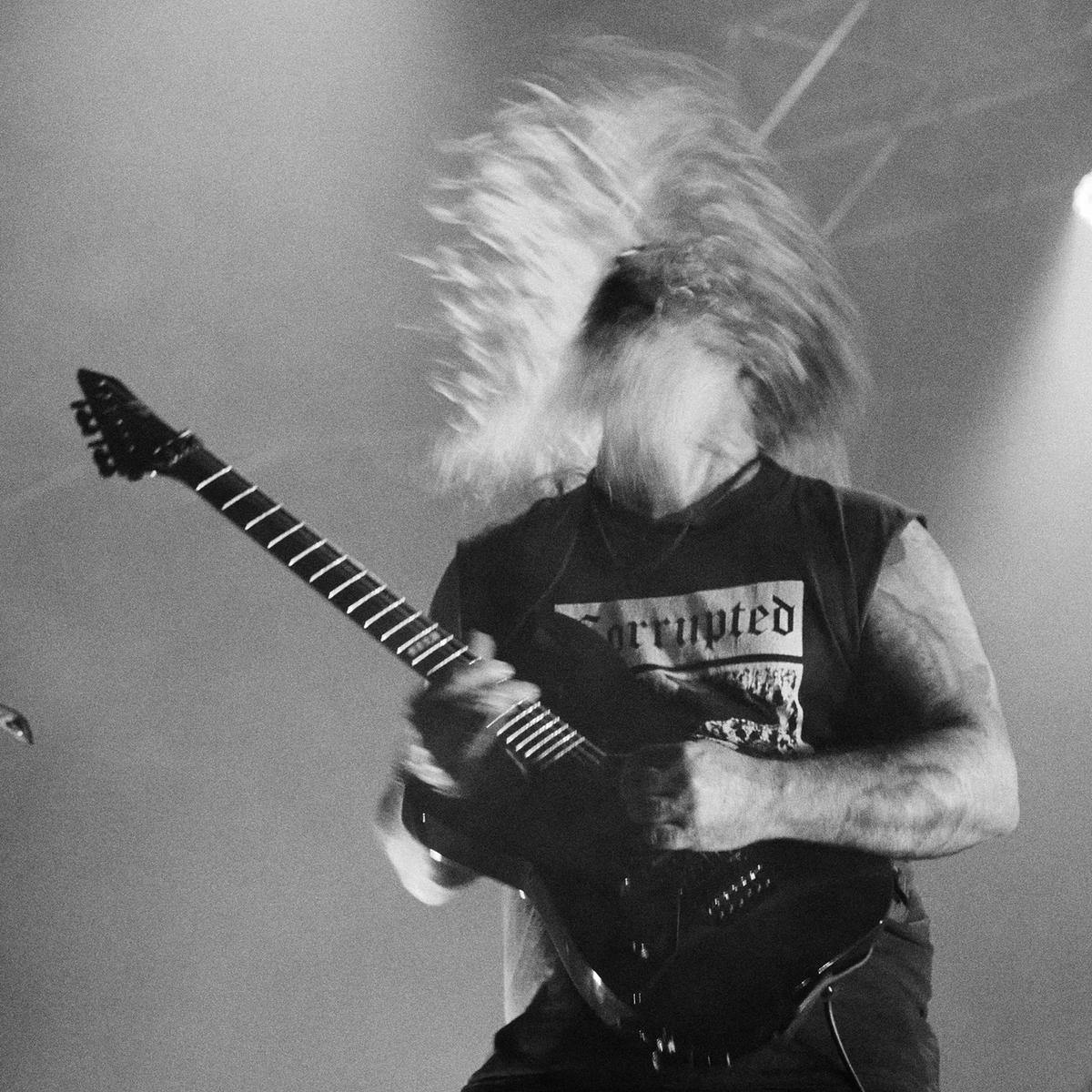 A black and white image of a guitar player, mid head-bang, their long hair flying around.