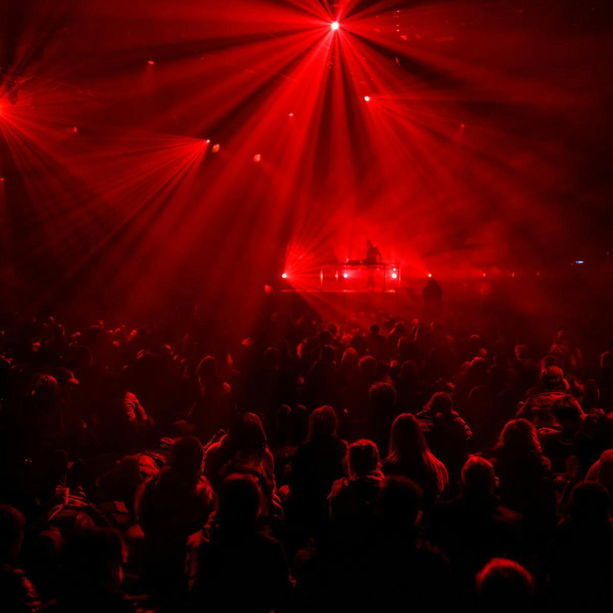 Hundreds of people bathed in red light as they watch a performer on stage.